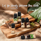 Set of essential oil bottles on a wooden board with text 'Let the Woods Welcome You Home' and natural elements.